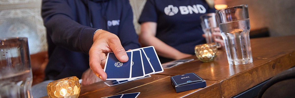 Menschen spielen BND-Kartenspiel in gemütlicher Runde – Beispiel für Branding, Brand Experience und Kundentouchpoint von brandingByMates.