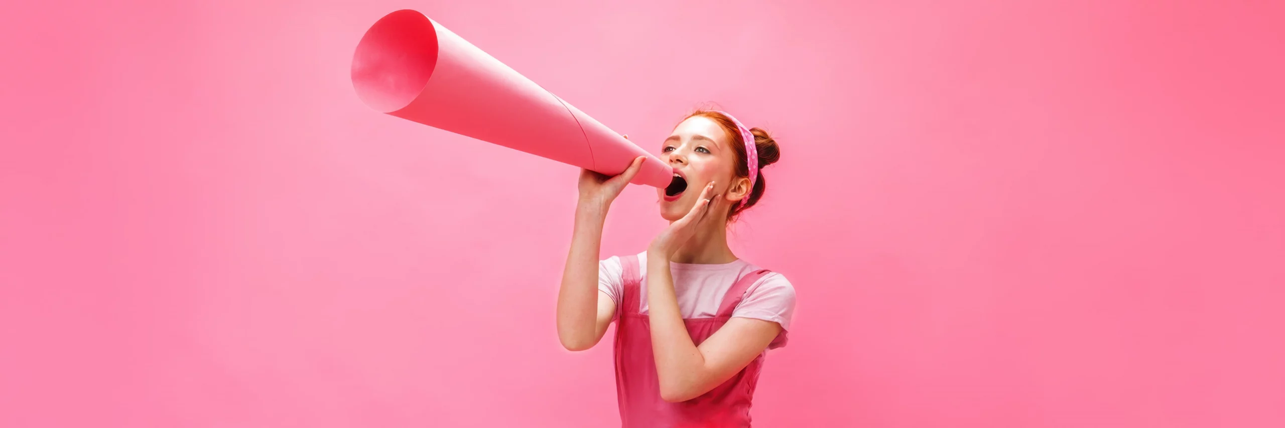 Frau ruft mit rosa Megafon vor rosa Hintergrund und symbolisiert Marketing Strategieentwicklung und gezielte Markenbotschaften.